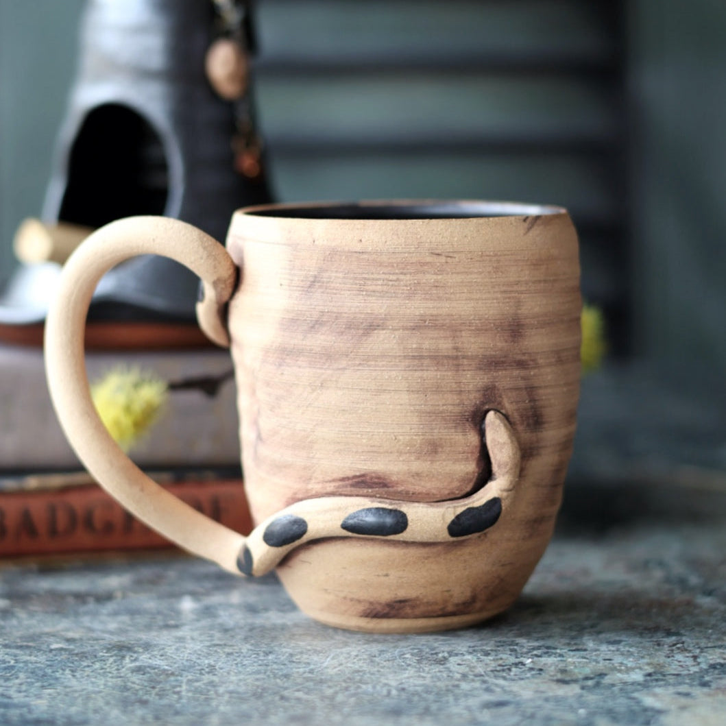 Handmade pottery  mug with a snake design on a textured surface