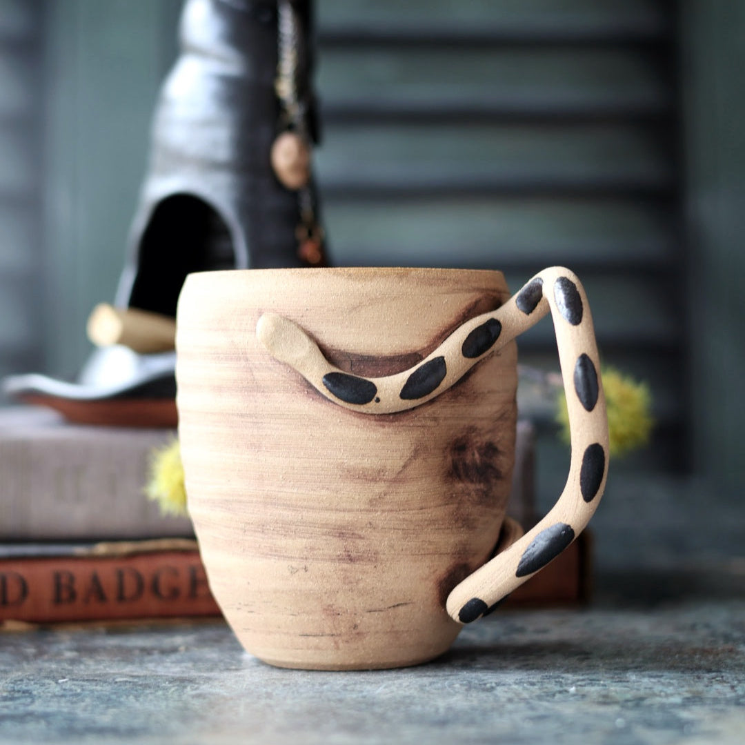 Ceramic mug with a unique handle design on a textured surface.